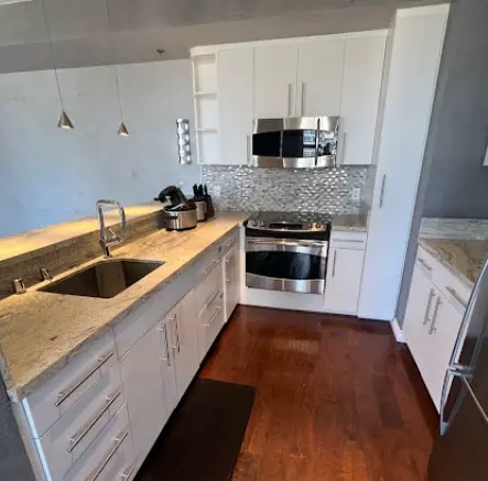 Cocina moderna con gabinetes blancos, encimeras de granito y electrodomésticos de acero inoxidable, mostrando un ambiente limpio y organizado.