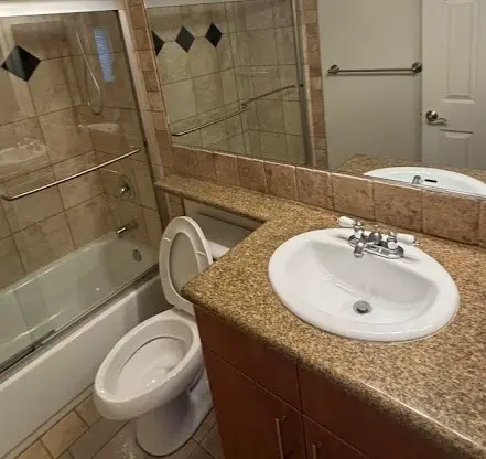 Baño con lavabo y espejo, inodoro y bañera con azulejos, todos los elementos perfectamente limpios y ordenados