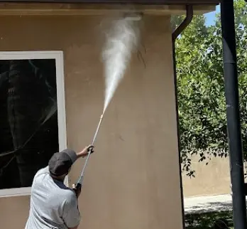 Empleado de Dust N Shine utilizando hidrolavadora para limpiar la pared exterior de una casa, eliminando suciedad y manchas