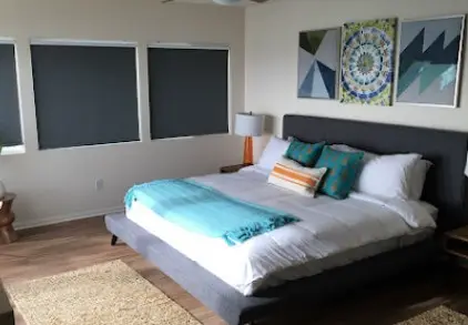 Dormitorio contemporáneo con cama de tamaño queen con cabecera gris, ropa de cama en tonos de azul y naranja, y cortinas oscuras para bloquear la luz, complementado con decoración de pared artística