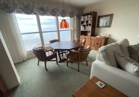 Sala comedor con vista al mar, decorada con muebles de madera y luz natural, ideal para un ambiente relajante.